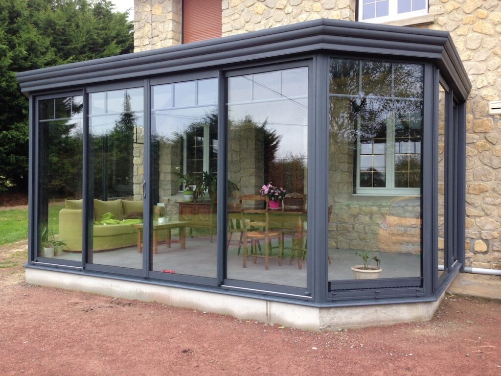 Extension de maison : véranda en aluminium gris anthracite avec baies vitrées coulissantes et mobilier de jardin.