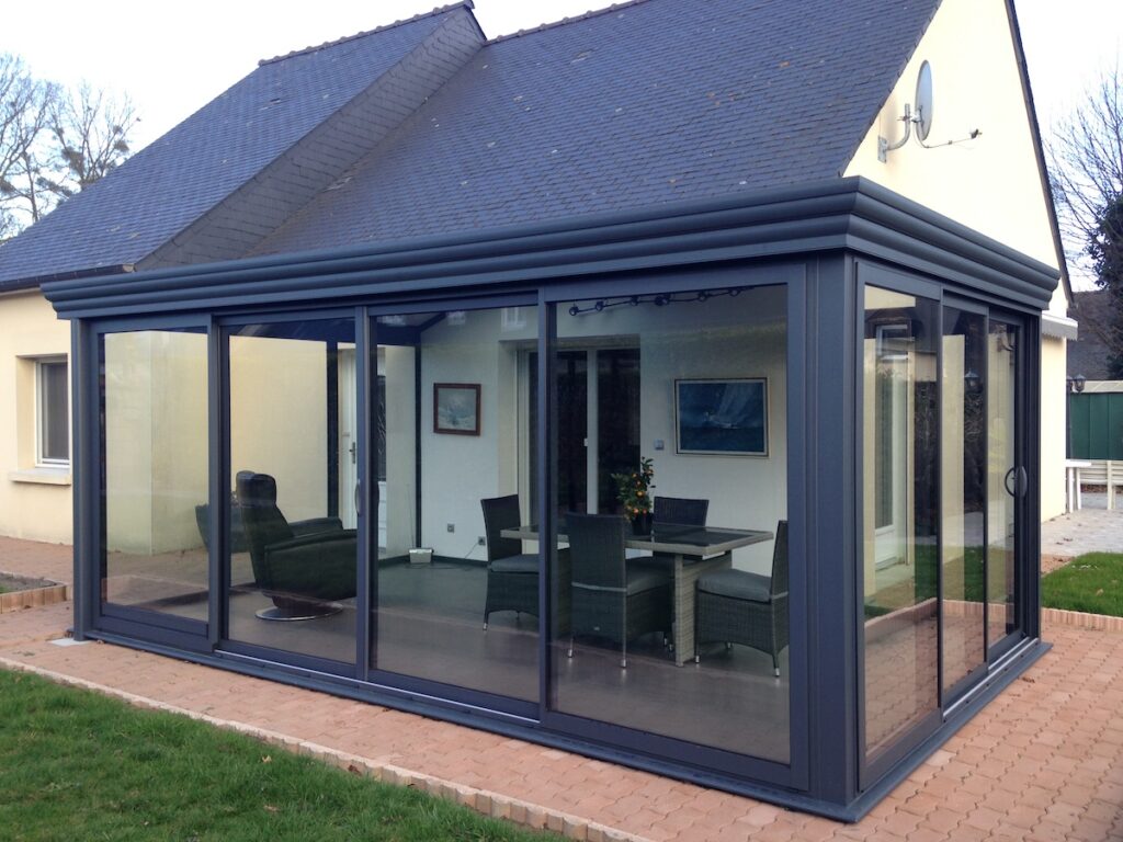 Véranda moderne anthracite avec baies vitrées coulissantes et mobilier de jardin, extension contemporaine de maison.