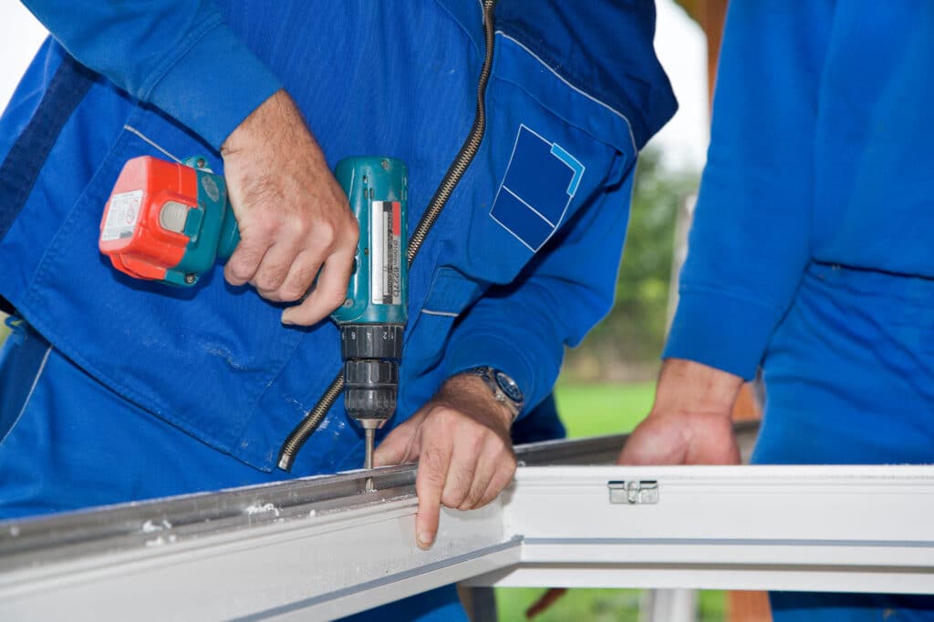 Menuisier utilisant une perceuse Makita 6227D pour fixer un châssis de fenêtre en PVC blanc.