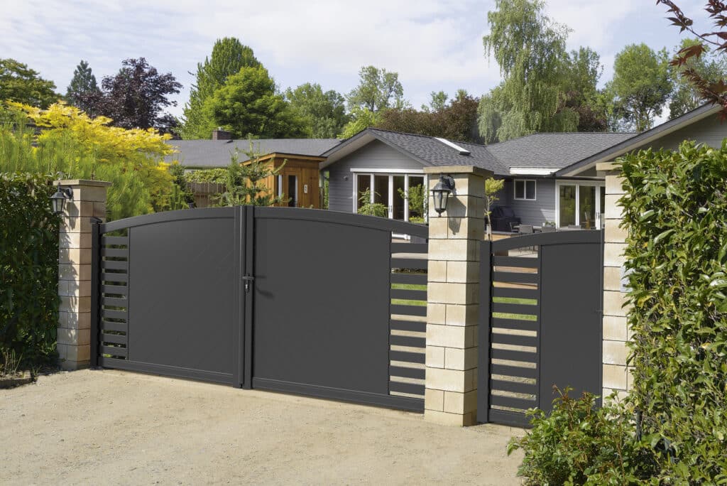Portail battant et portillon gris anthracite moderne devant une maison avec jardin et piliers en pierre.
